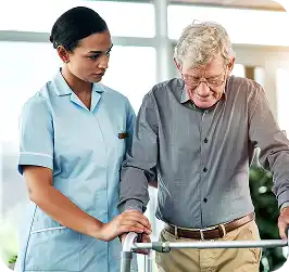 Nurse in light blue scrubs helping an older man who uses a walker